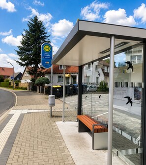Un arrêt de bus équipé d’un abri, d’un banc et d’un panneau indiquant la direction à suivre pour rejoindre Vellmar Ansprey.