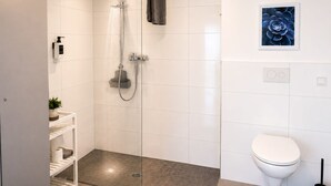 A modern bathroom with a glass-enclosed shower, a white toilet, and a shelf with toiletries. - Stylish apartment: quiet, 24/7 self check-in & Wi-Fi, street parking (Göttingen)