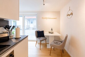 Une cuisine moderne avec un grille-pain PHILIPS, une table blanche sur laquelle se trouvent un saladier et une bouteille de vin, ainsi que deux chaises.