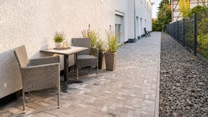 An outdoor patio area with wicker furniture, potted plants, and a paved walkway. - Stylish apartment: quiet, 24/7 self check-in & Wi-Fi, street parking (Göttingen)