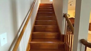 A wooden staircase with a handrail, leading to an upper floor. - Peaceful Lakefront Living – 3-BR Home with Breathtaking Views; Pet & Smoke-Free (Charter Township of Berlin)