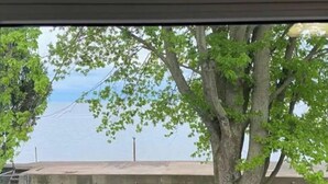 A tree-lined view with a concrete building in the background. - Peaceful Lakefront Living – 3-BR Home with Breathtaking Views; Pet & Smoke-Free (Charter Township of Berlin)