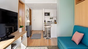 A modern living room with a flat-screen TV, a blue sofa, and a kitchen area with white cabinets and a microwave. - ALTIDO Apartamento luminoso na zona sossegada do Porto, perto do Mercado Bom Suc (Porto)