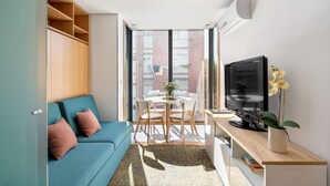 A modern living room with a blue sofa, a TV on a wooden stand, and a dining area with a table and chairs. - ALTIDO Apartamento luminoso na zona sossegada do Porto, perto do Mercado Bom Suc (Porto)