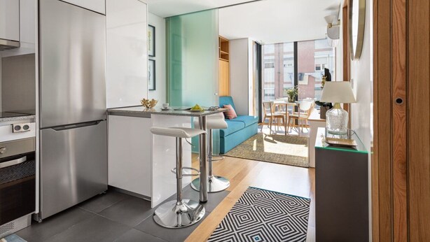 A modern kitchen with a stainless steel refrigerator, white cabinets, and a bar stool. - ALTIDO Apartamento luminoso na zona sossegada do Porto, perto do Mercado Bom Suc (Porto)
