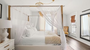 Ein Schlafzimmer mit Himmelbett, Nachttisch mit Lampe und Blick ins Freie durch ein Fenster.