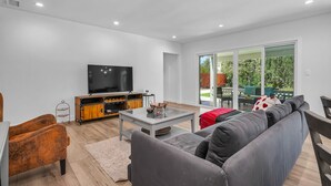 Una sala moderna con un televisor de pantalla plana, un mueble de entretenimiento de madera, un sofá gris y una mesa de centro de vidrio.