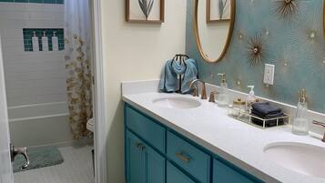 Une salle de bain avec un lavabo blanc, des meubles turquoise, un grand miroir et un mur décoratif orné de motifs en forme d’étoiles.