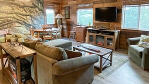 Ein gemütliches Wohnzimmer mit Sofa, Couchtisch und Fernseher. Holzvertäfelte Wände und eine Steinwand.