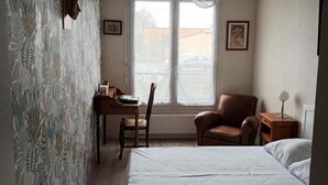 A bedroom with a bed, a desk, a chair, and a window with a view of the outside. - L'Intemporel - Appartement T3 avec jardinet - 3* (Poitiers)