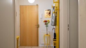 A hallway with a wooden door, a radiator, a small yellow table with a vase of flowers, and a yellow coat rack with an umbrella. - L'Intemporel - Appartement T3 avec jardinet - 3* (Poitiers)