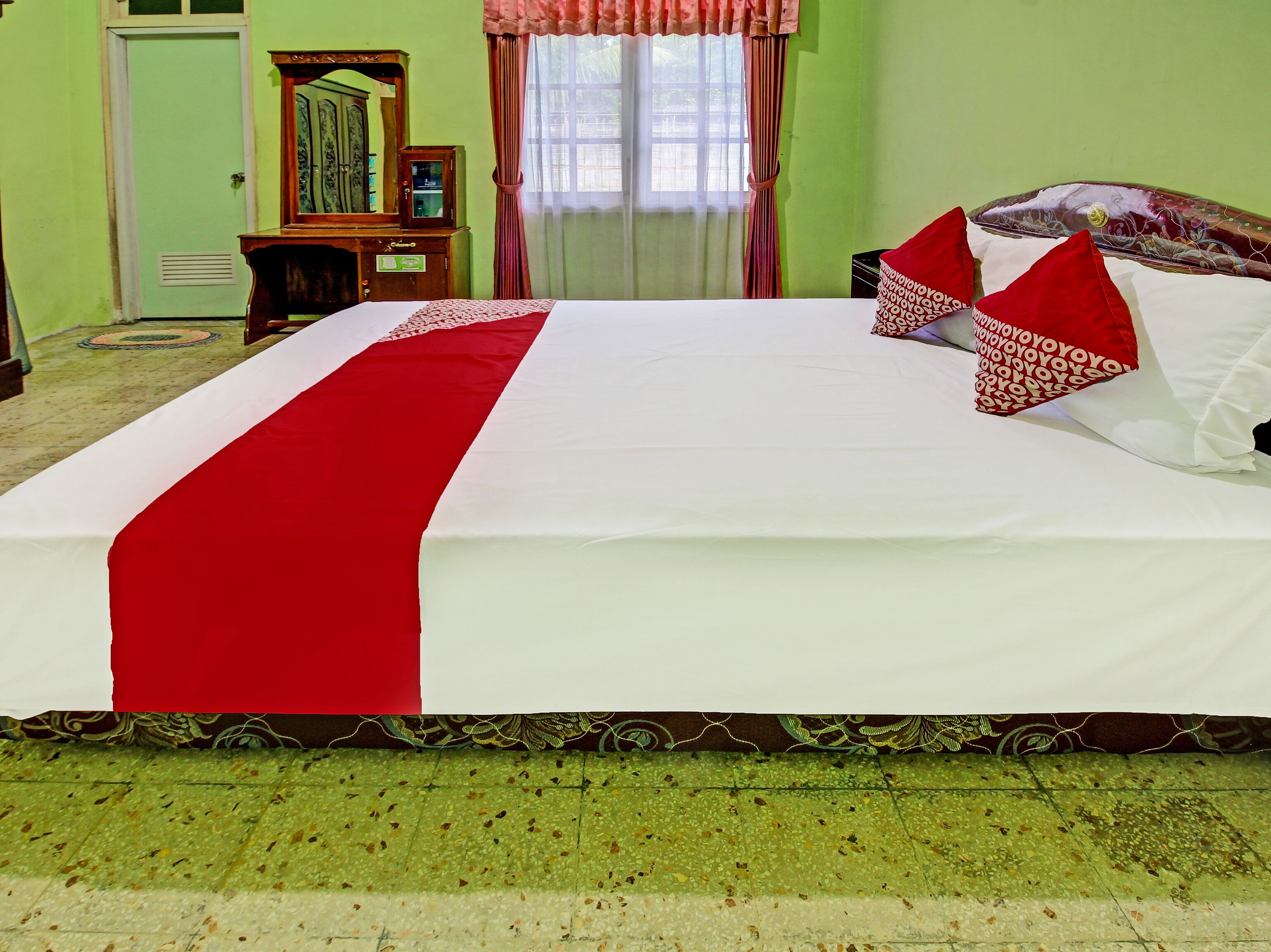 Un lit bien fait, recouvert d’une couvre-lit rouge et blanche, avec deux oreillers rouges et une tête de lit en bois.