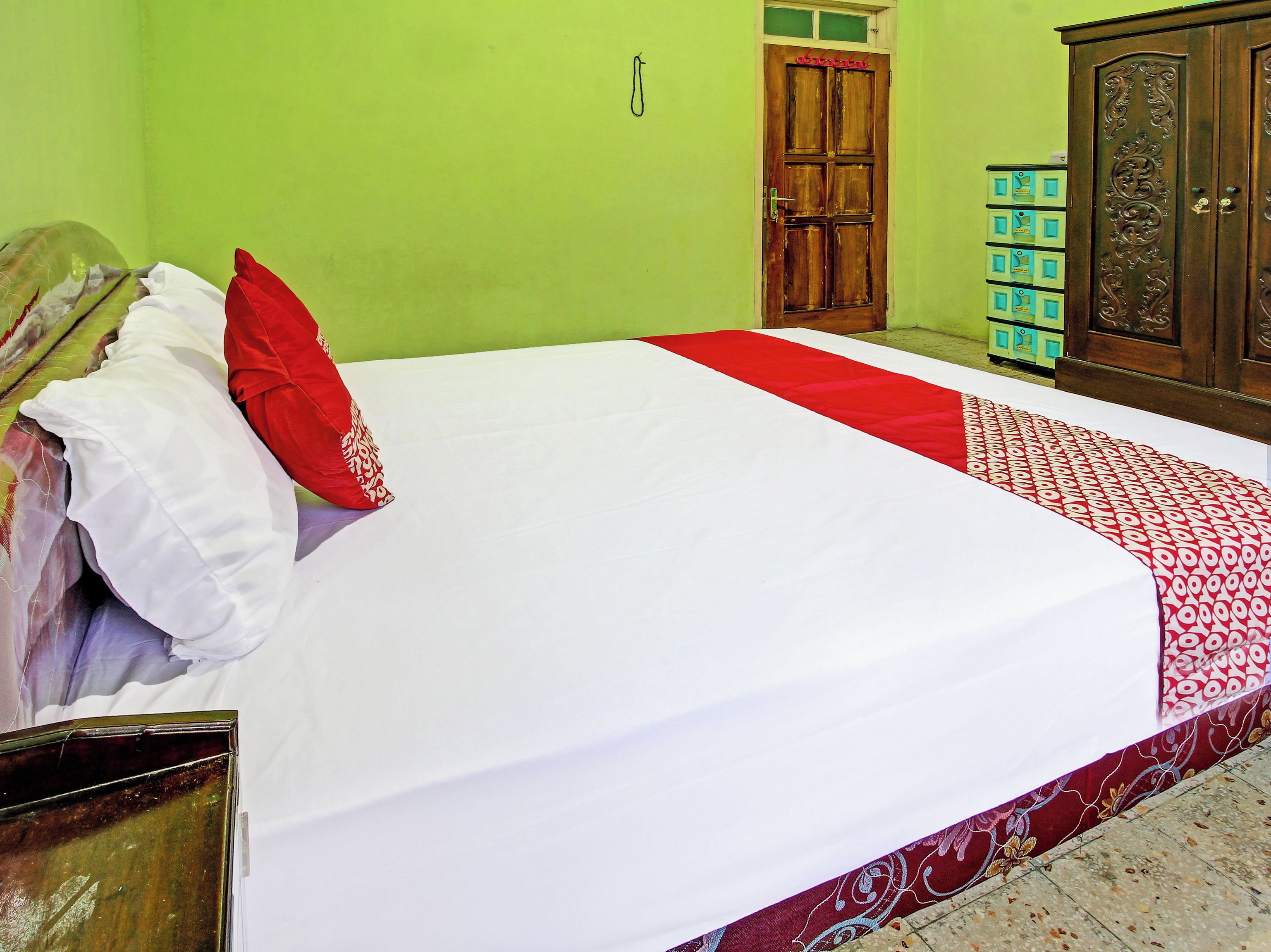 A neatly made bed with white and red bedding, a wooden wardrobe, and a green wall.