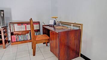 Una habitación con un escritorio de madera, una silla, una estantería y una pequeña mesa con una lámpara.
