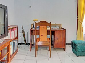 Ein Zimmer mit Schreibtisch aus Holz, einem Sessel, einem Fernseher und einem Bücherregal.