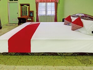 Ein ordentlich bezogenes Bett mit einer roten und weißen Tagesdecke, zwei roten Kissen und einem hölzernen Kopfteil.