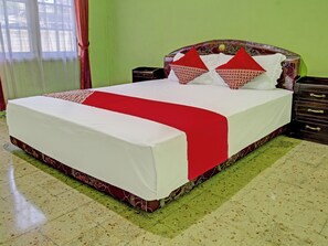 Ein ordentlich bezogenes Bett mit einer roten und weißen Tagesdecke, einem gemusterten Kopfteil und einer grünen Wand.