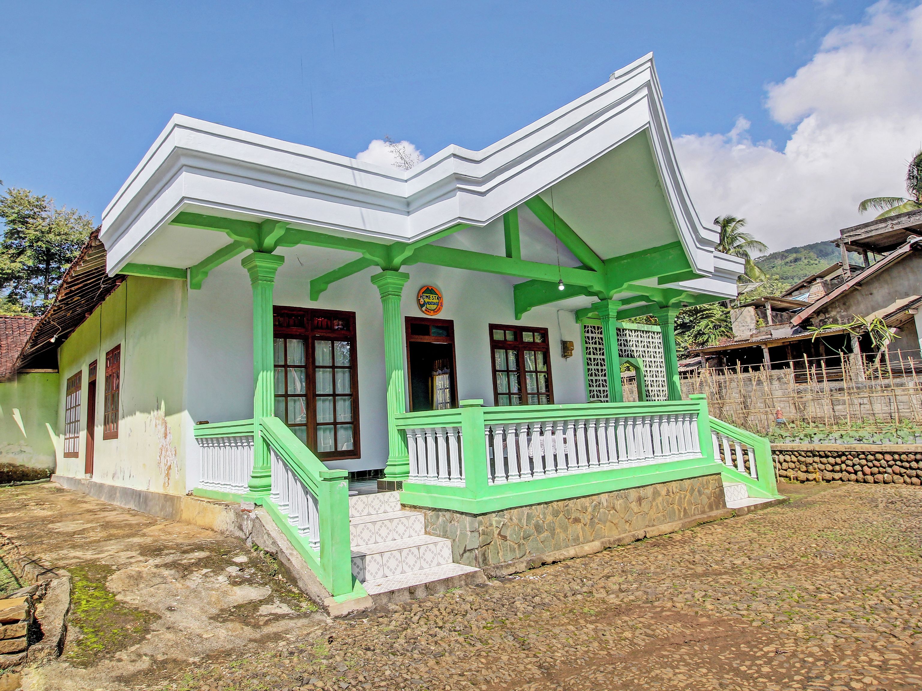 A traditional house with a green and white color scheme, featuring a porch with a staircase leading to the entrance.