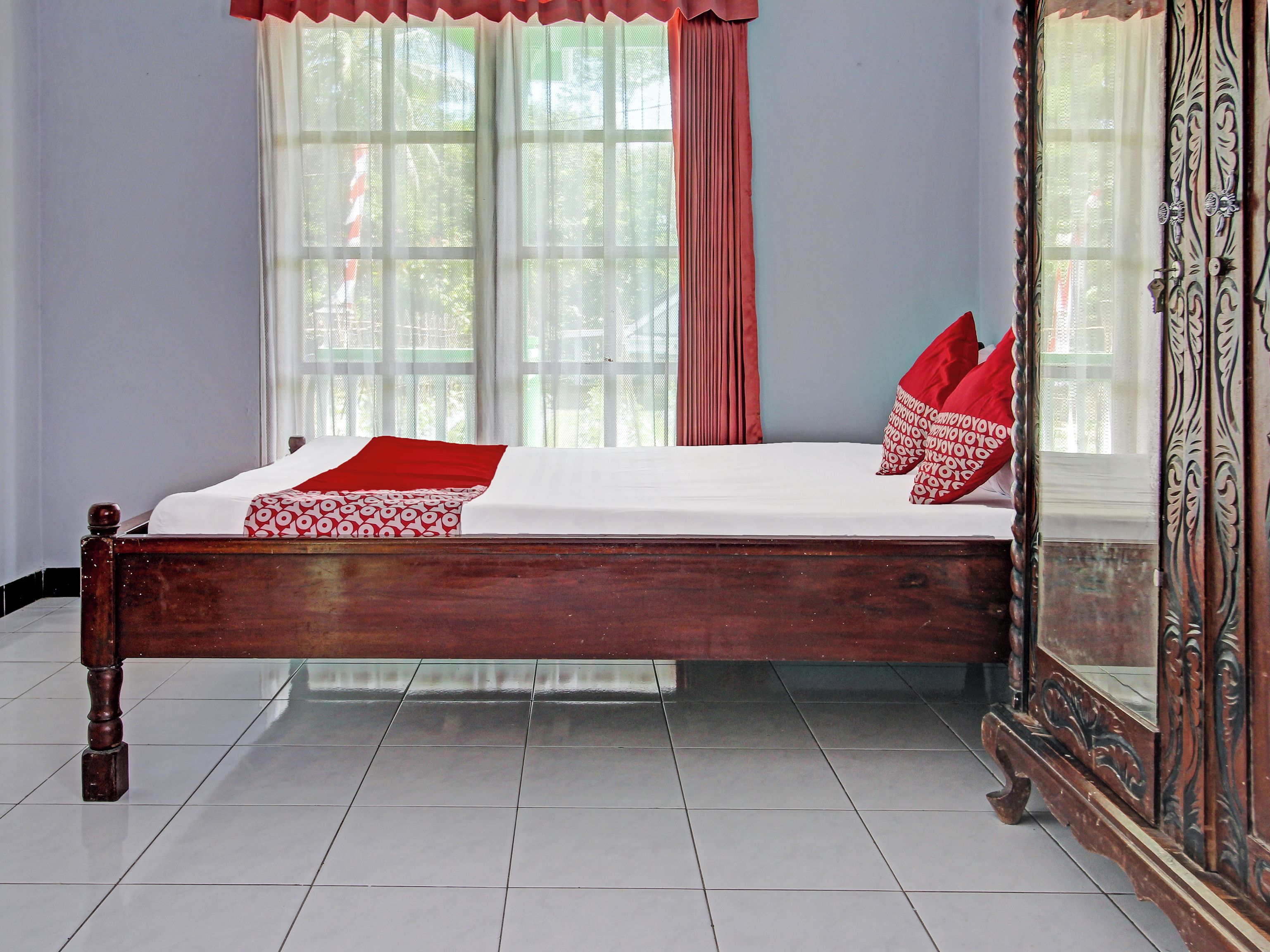 Una cama con estructura de madera, ropa de cama blanca y almohadas rojas.