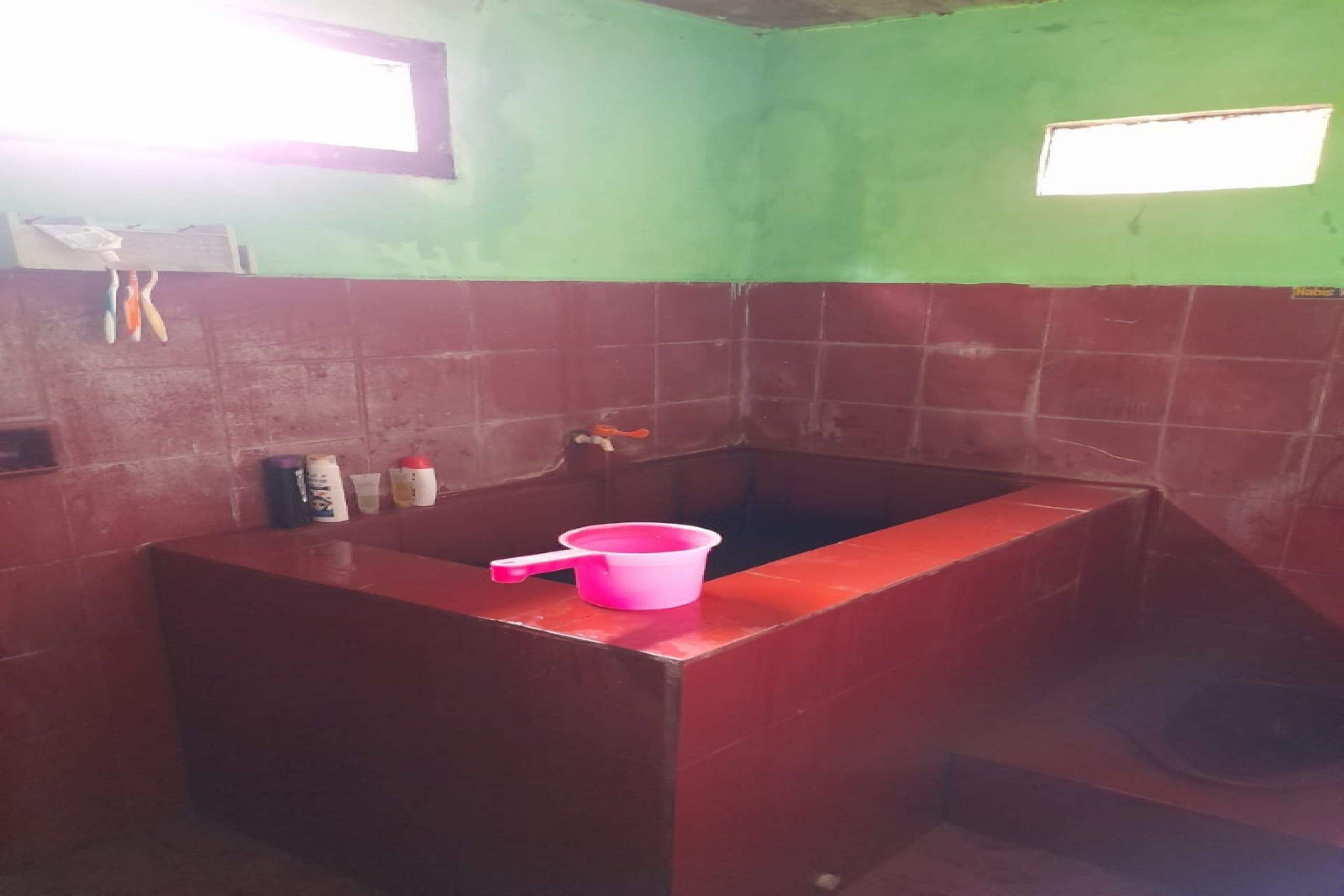 A bathroom with a red sink, a pink basin, and a window.