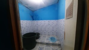Une petite salle de bain avec un sol carrelé en bleu et blanc, un seau noir et un abattant de toilettes bleu.