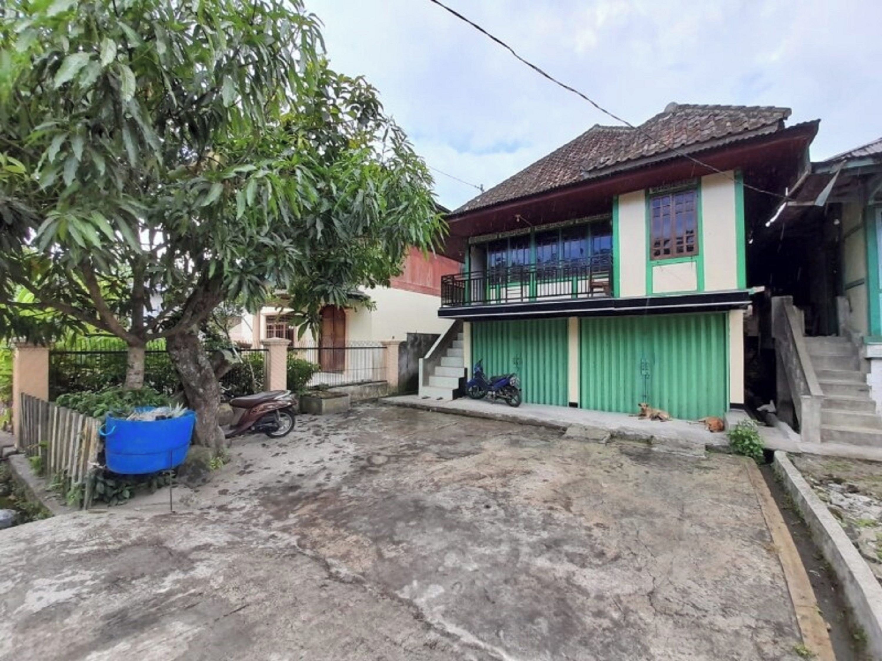A residential building with a green garage door, a balcony, and a tree in the yard.