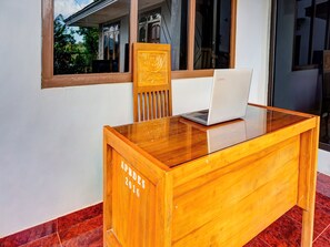Un bureau en bois avec un ordinateur portable, une chaise et une fenêtre donnant sur un immeuble et des arbres.