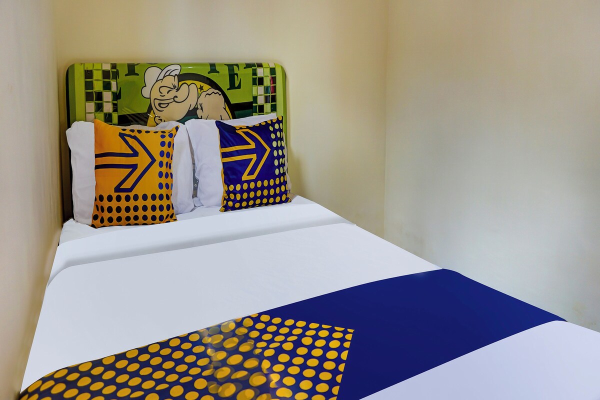 Un lit avec un matelas blanc, une couvre-lit à motifs bleus et jaunes, et trois oreillers aux motifs géométriques.