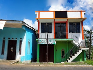 Un bâtiment à deux étages, sur lequel on peut lire l’enseigne « Café Miki Kosuka Papafood’s », et un escalier menant à l’étage supérieur.