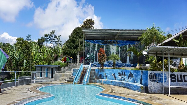 Une piscine agrémentée d’une fresque murale, d’un toboggan et d’un espace couvert offrant une vue sur la fresque.