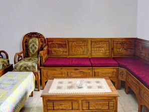 A room with a wooden sofa with intricate carvings, a matching wooden armchair, a small wooden table with a lace tablecloth, and a bed with a floral bedspread. - OYO Homes 91132 Desa Wisata Kalipucang (Purwosari)