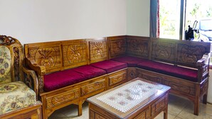 Un canapé traditionnel en bois, orné de sculptures complexes, un fauteuil assorti et une petite table recouverte d’une nappe en dentelle.