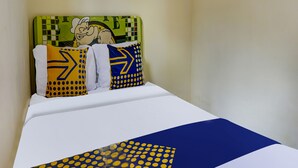 Un lit recouvert d’une couvre-lit blanche et bleue, deux oreillers ornés de motifs jaunes et bleus, et une tête de lit verte décorée d’un personnage de dessin animé.