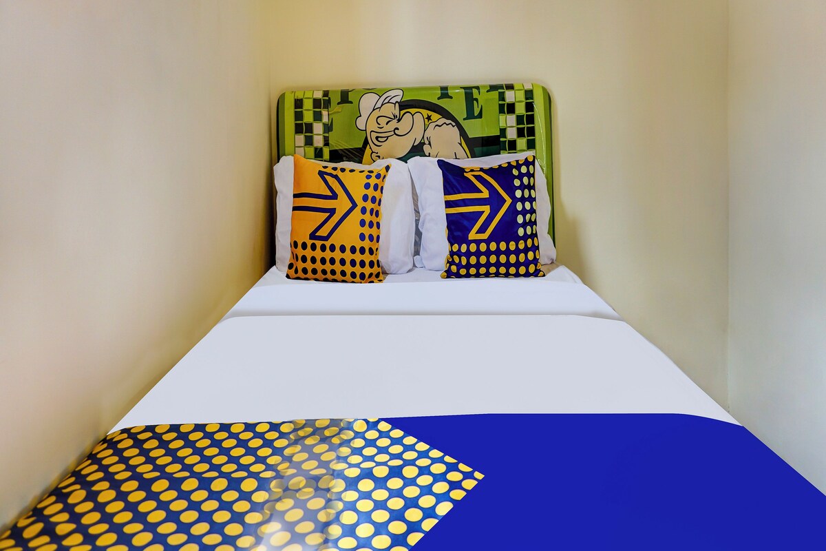 A bed with a white mattress and a blue and yellow patterned blanket. There are two pillows with yellow and blue designs.