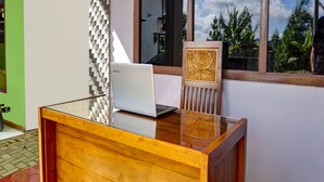 Un bureau en bois avec un ordinateur portable, une chaise au motif sculpté et une fenêtre donnant sur un paysage verdoyant.