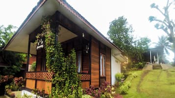 A wooden house with a porch, surrounded by lush greenery and a well-maintained lawn.