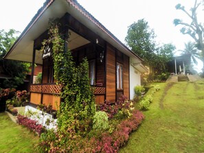 Ein hölzernes Haus mit Veranda, umgeben von üppigem Grün und einem gepflegten Rasen.