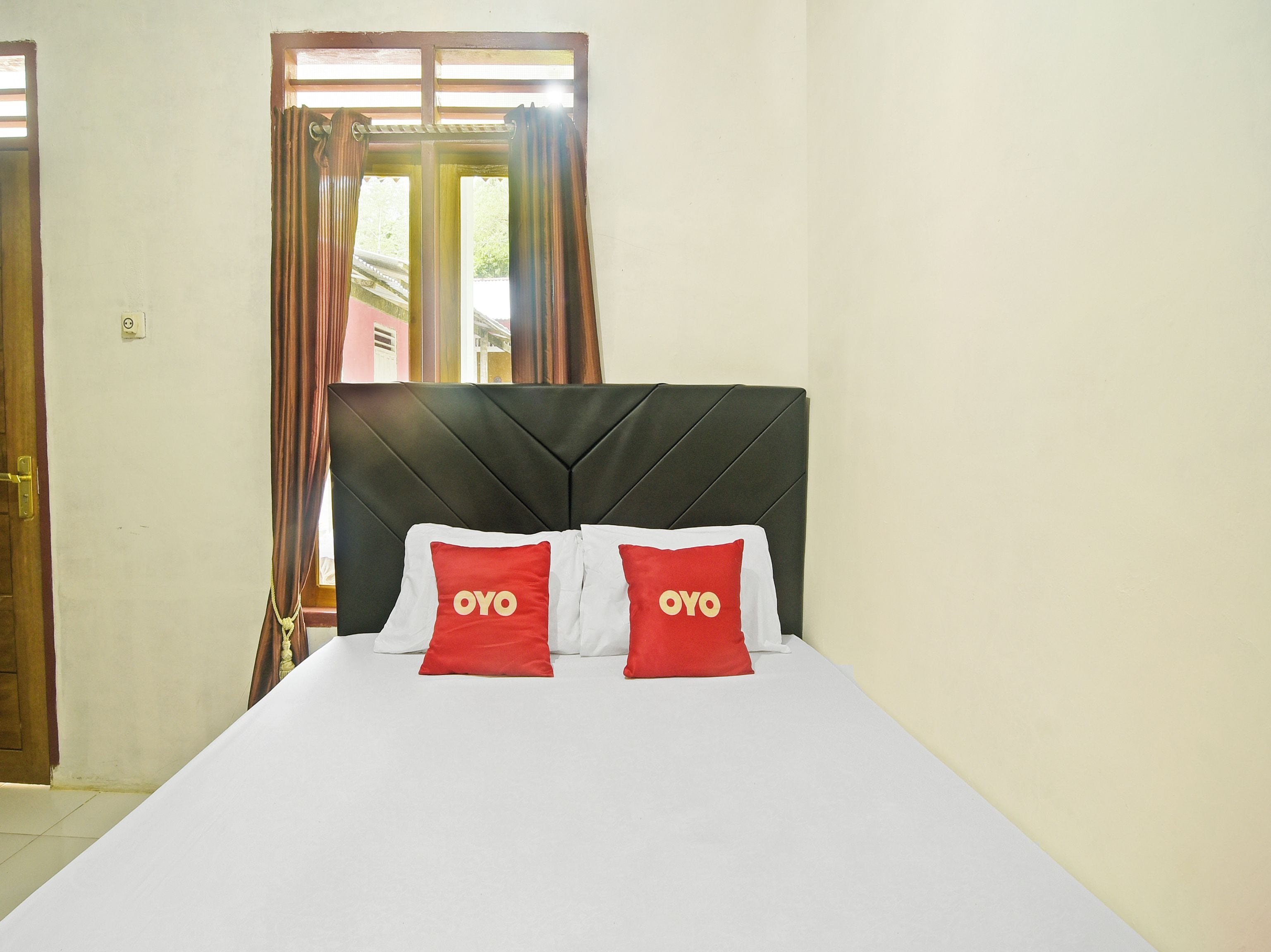 A hotel room with a bed, a headboard, curtains, and a window.