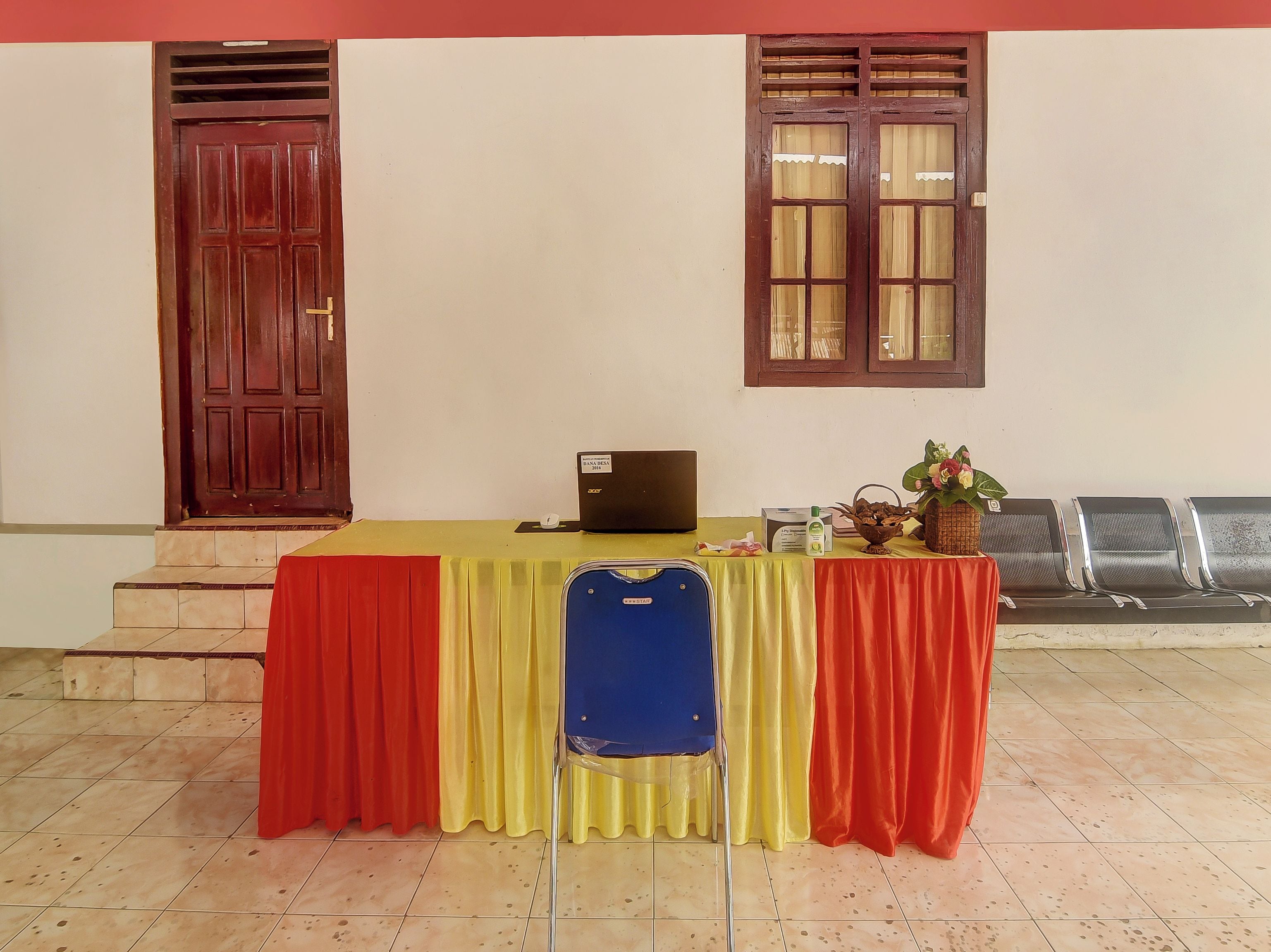 A room with a table set up for a meeting, a laptop, a blue bag, and a plant on the table.