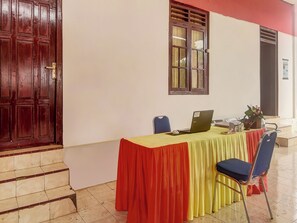 Une pièce avec une porte en bois, une fenêtre avec un rideau, une table avec un ordinateur portable, une chaise et une petite plante.
