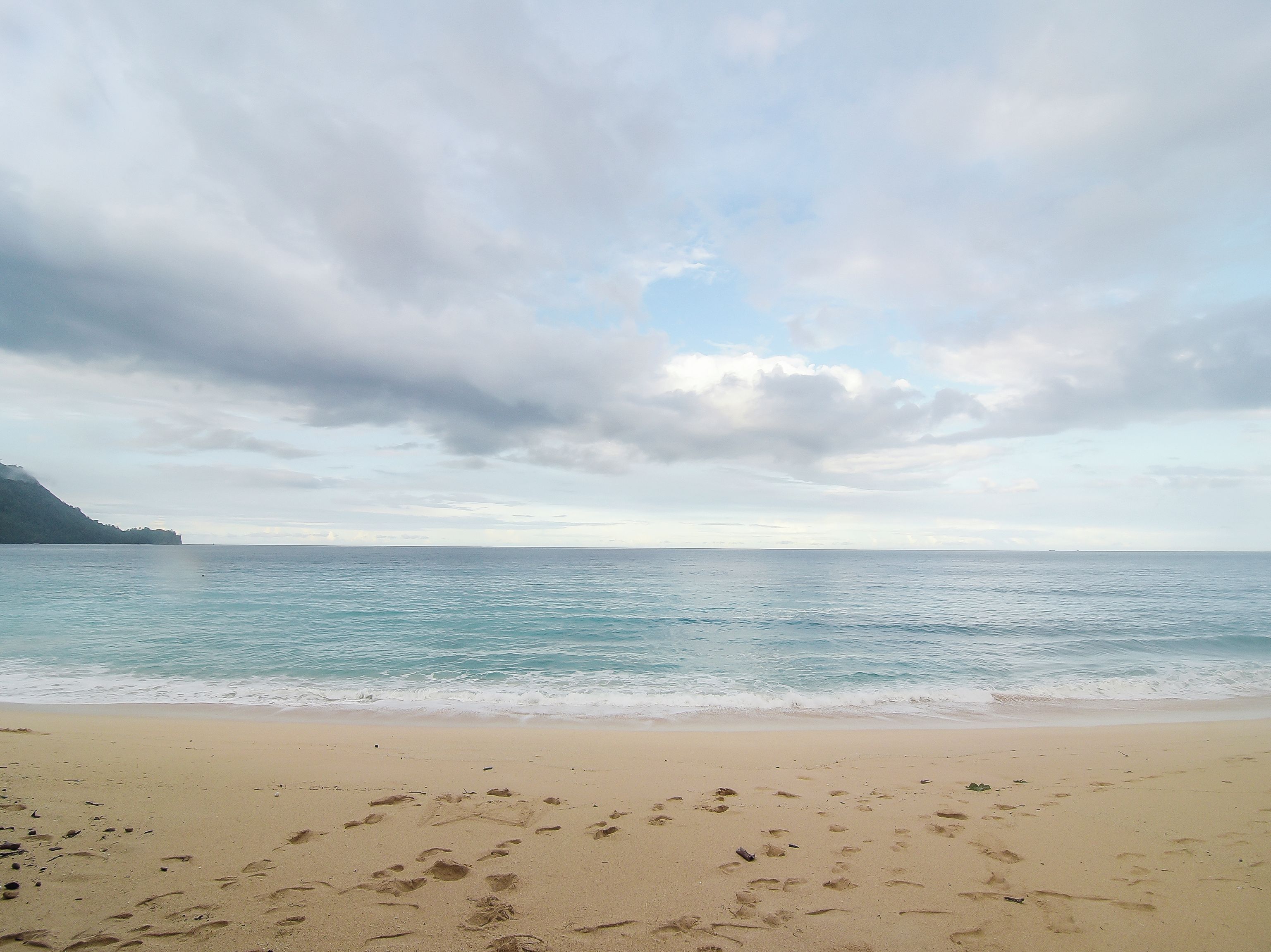 A beach with footprints in the sand and a cloudy sky.