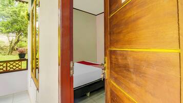 A room with a bed, a window with a view of greenery, and a door with a QR code.