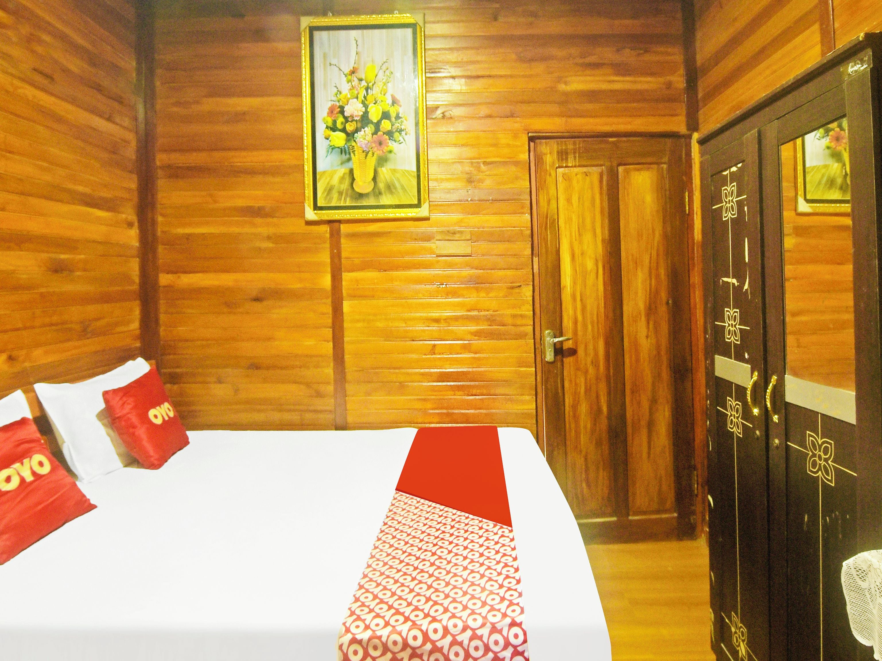 A wooden-paneled room with a bed, pillows, a door, and a framed picture on the wall.