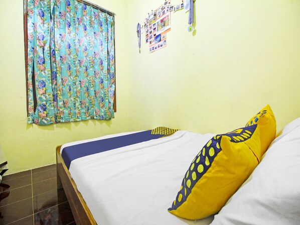 A bed with white and blue bedding, a yellow pillow with blue patterns, and a floral curtain on a light yellow wall.