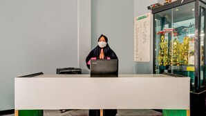 A reception desk with a person standing behind it, a glass display case with trophies, and a wall with a list of names. - OYO 90997 Eco Desacibodasbabakangentong2syariah (Lembang)
