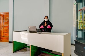 Un comptoir d’accueil avec un ordinateur portable, une personne vêtue de noir et de rose, et un présentoir à trophées.