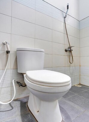 A bathroom with a white toilet, a shower head, and tiled walls. - OYO 90935 Rumah Kost Metroliving (Surabaya)