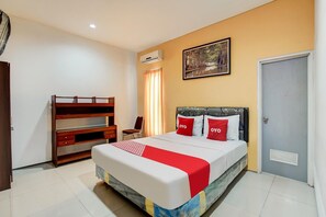 A bedroom with a bed, a desk, a chair, an air conditioner, a door, and a painting on the wall. - OYO 90935 Rumah Kost Metroliving (Surabaya)