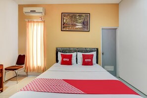 A hotel room with a bed, a chair, an air conditioning unit, a door, and a painting on the wall. - OYO 90935 Rumah Kost Metroliving (Surabaya)