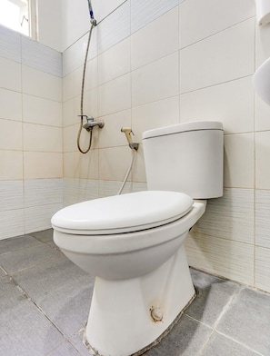 A white toilet with a shower head mounted on the wall, tiled walls, and a tiled floor. - OYO 90935 Rumah Kost Metroliving (Surabaya)